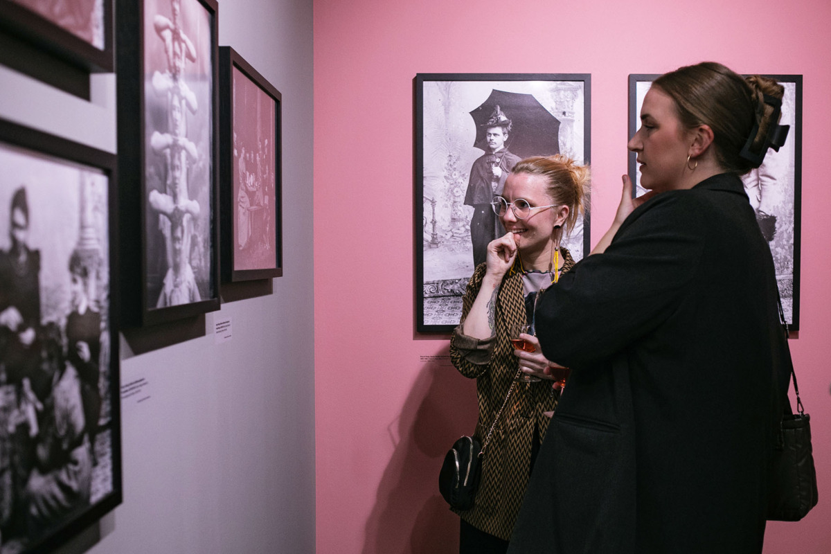 Zwei Besucherinnen betrachten die Bilder der Ausstellung LIKE A WHIRLWIND – Die Genderplays von Marie Høeg & Bolette Berg